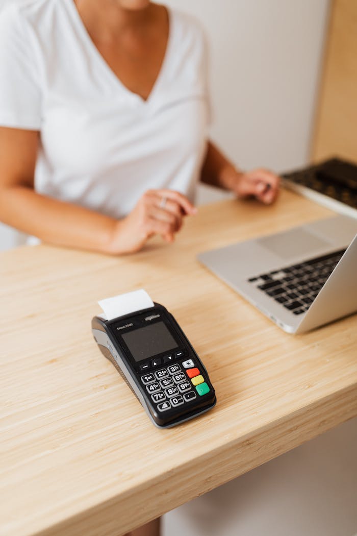 About A cashier processes a cashless transaction using a payment terminal and laptop at a retail counter.