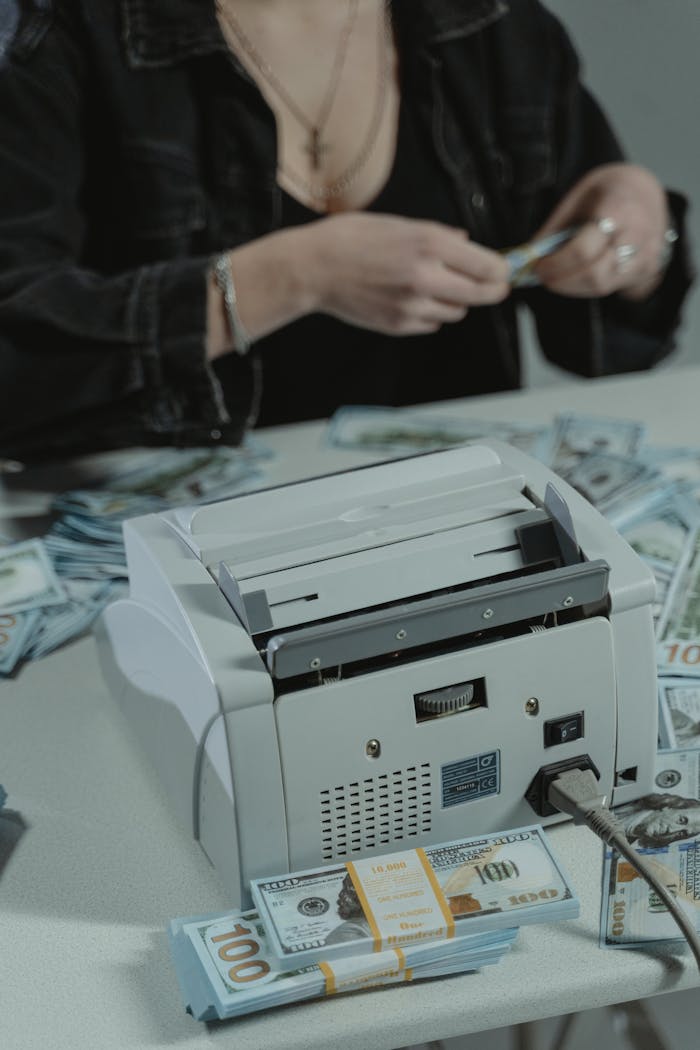 Services Woman using a money counter to count US dollar bills on a table.