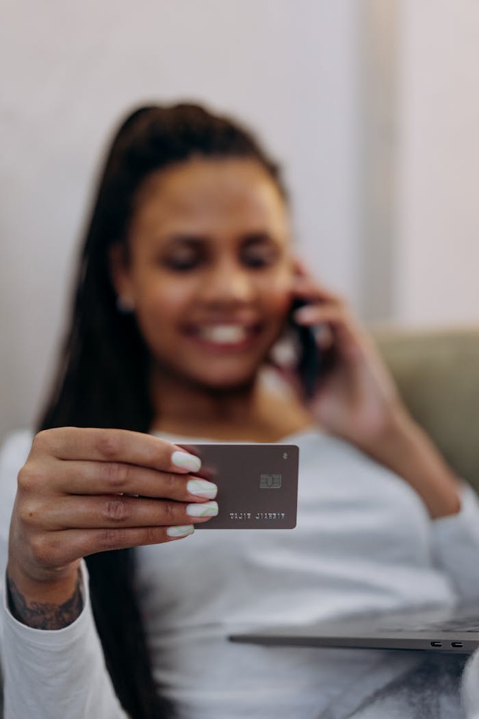 Mastering the First Impression: Your intriguing post title goes here Focused shot of a woman holding a credit card, engaging in a phone conversation, depicting online shopping or banking.