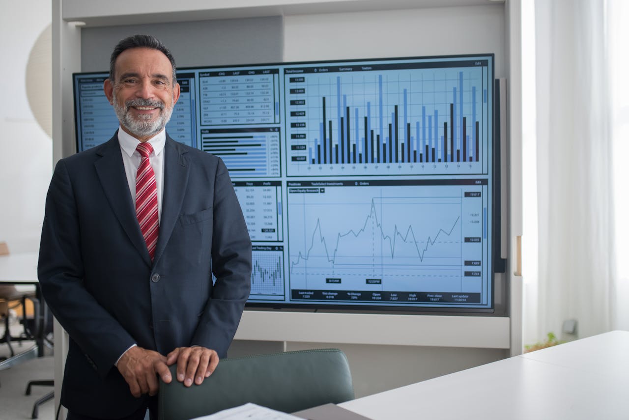 About Smiling businessman in office analyzing financial graphs on a large screen, demonstrating professional success.